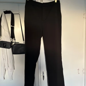 Svarta kostymbyxor från Gina Tricot - Säljer ett par klassiska svarta kostymbyxor från Gina Tricot. Byxorna har normal passform, hög midja och stängs med dragkedja och knapp. Aldrig använda 