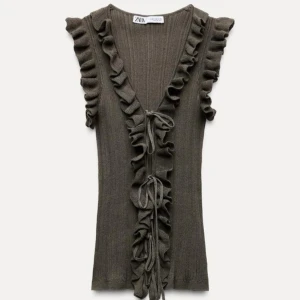 Brun ribbad topp med volang från Zara - Supersnygg brun ribbad topp från Zara med volangdetaljer längs ärmhål och framkant. Djup v-ringning och knyt framtill ger en trendig look. Perfekt att styla med jeans eller kjol.💗💗