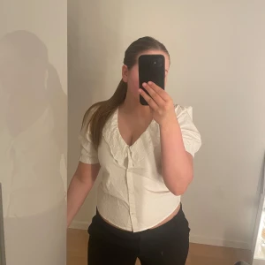 Vit blus med broderad krage - Säljer en söt vit blus med korta puffärmar och stor broderad krage. Blusen har v-ringning och knäpps framtill med knappar. Säljer då den häng i garderoben ett tag och då blivit för liten🩷