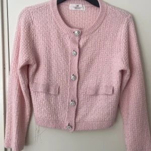 Ljusrosa stickad kofta från H&M - Ljusrosa stickad kofta från H&M med glittriga knappar framtill och två dekorativa fickor. Koftan har lång ärm och rund halsringning. Skriv om ni vill ha mer information om tröjan 🩷tar emot diskutering om pris!