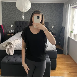 Svart blus - Svart blus eller T-shirt aktig med volangärmar från Flash Woman, strl M. Känns som en T-shirt men volangärmarna är av annat material