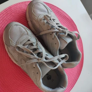 Grå sneakers från Lejon - Säljer ett par grå sneakers från Lejon i storlek 37. Skorna har snörning och är tillverkade i syntetmaterial med meshpaneler för extra andningsförmåga. Perfekta för dig som gillar en sportig och stilren look. Köpta på skopunkten och är näst som nya. Provade och använda en gång men. Inget kvitto så kan tyvärr inte lämna tillbaka dom. 