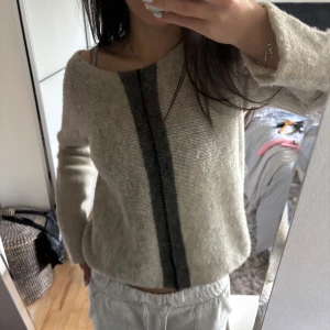 Grå stickad tröja med grå rand - Säljer en beige stickad tröja med en bred grå rand framtill. Tröjan har lång ärm och en lite lös passform. Perfekt för dig som gillar en enkel men snygg stil.
