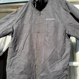 Svart vindjacka från Columbia - Säljer en svart vindjacka från Columbia med dragkedja framtill och diskret logga på bröstet. Jackan har lång ärm och praktiska fickor. Perfekt för blåsiga dagar och enkel att matcha med olika outfits.