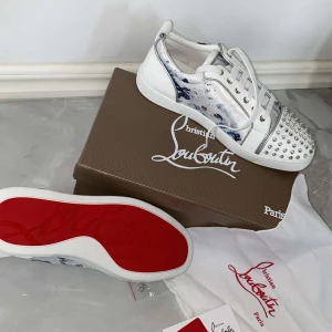 Christian Louboutin Lou Spikes Orlato sneakers - Säljer ett par Christian Louboutin Lou Spikes Orlato sneakers i vitt med blå detaljer och silverfärgade nitar framtill. Skorna har den klassiska röda sulan och snörning. Perfekta för dig som vill sticka ut med exklusiva detaljer och unik design.