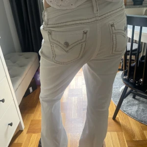 Vita jeansbyxor från miss me - Säljer ett par vita jeansbyxor från True Religion med dekorativa sömmar och silverfärgade knappar. Byxorna har klassiska bakfickor med logga och raka ben. Perfekta för dig som vill ha en stilren och trendig look.