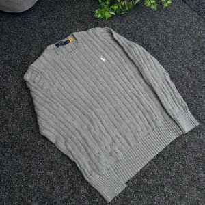 Grå kabelstickad tröja från Polo Ralph Lauren - Säljer en klassisk grå kabelstickad tröja från Polo Ralph Lauren med rund halsringning och broderad logga på bröstet. Tröjan är tillverkad i bomull och har långa ärmar samt ribbade muddar vid ärmslut och nederkant. Passar bättre M‼️‼️🚨🚨