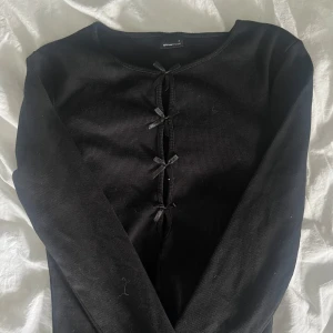 Topp med rosetter  - Svart långärmad ribbad topp från Gina Tricot med rosetter framtill. Aldrig kommit till användning. För fler bilder eller info, kom privat💖