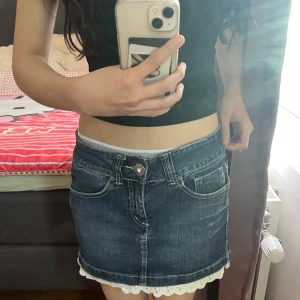 Jeanskjol med spetskant - Säljer en klassisk blå jeanskjol med söt vit spetskant längst ner. Kjolen har normal passform, fem fickor och knapp- samt dragkedjestängning framtill. Perfekt för dig som gillar en enkel men ändå söt stil.