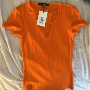 Topp  - Trendig orange ribbad topp från Bik Bok med unik cut-out detalj och knapp framtill. Kortärmad och figurnära passform, perfekt för att sticka ut med en färgklick i garderoben.