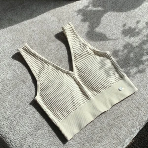 Beige ribbad linnetopp från DOM - Snygg beige ribbad linnetopp från DOM med djup v-ringning och bred resår nedtill. Perfekt att styla till jeans eller kjol för en trendig look.