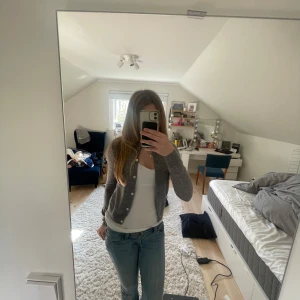 Grå kofta från MNG - Säljer en enkel och stilren grå kofta från MNG. Koftan har långa ärmar, rund halsringning och knäppning framtill med små knappar. Perfekt att slänga över en topp eller t-shirt för en avslappnad look. Bara använt fåtal gånger och pris kan diskuteras 