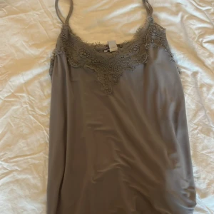 Grå linnetopp med spets från New Yorker  - Säljer en grå linnetopp från New Yorker med tunna axelband och vacker spetsdetalj längs urringningen. Toppen har en mjuk och följsam känsla, perfekt för att skapa en stilren look. Säljer pågrund av dålig användning.💖