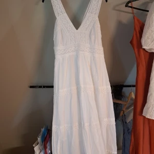 Vit medellång klänning med fina spetsdetaljer - Superfin vit medellång klänning med v-ringning och broderad topp i storlek S/M. Klänningen har vackra spetsdetaljer upptill och i midjan! Perfekt för sommarens alla tillfällen☀️