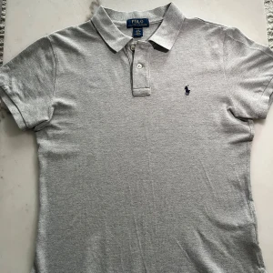 Polo Ralph Lauren Grå Tröja - Säljer en stilren och klassisk grå Tröja från Ralph Lauren i storlek S. Den har en tidlös design med diskret broderad logga på bröstet och passar perfekt både till vardags och en mer avslappnad stil. T-shirten är i fint skick och priset kan diskuteras vid seriöst intresse.