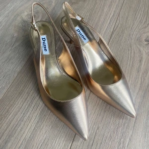 Pumps med spetsig tå  - Säljer ett par pumps i guld från Dune med spetsig tå och låg klack. Skorna har öppen häl med justerbart spänne och glansig finish. Endast testade🩷