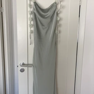 Ljusgrön långklänning med draperad urringning - Säljer en elegant ljusgrön långklänning med smala axelband och draperad v-ringad urringning. Klänningen har en mjuk satinliknande yta och en figurnära passform som faller snyggt längs kroppen. Perfekt för speciella tillfällen.