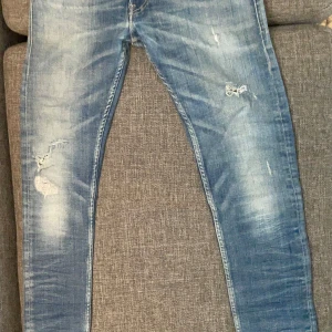 Replay Slim Blue Jeans - Säljer ett par Replay Jondrill jeans i blå tvättad denim med slitningar och detaljerade sömmar. Byxorna har smal passform, klassiska fem fickor och logotyp på bakfickan. Perfekta för dig som gillar en modern och lite tuffare stil.