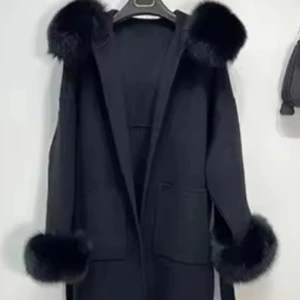 Svart kappa med äktapälsdetaljer - Säljer en svart kappa med stora äktapälsdetaljer på huva och ärmslut. Jackan har två fickor framtill och ett bälte i midjan, ena sidan av trådbanden som bälte går genom har gått sönder men går att fixa annars så kan du bara knyta bältet över de annars är kappan som ny