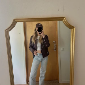 Vinröd skinnjacka - Säljer en vinröd skinnjacka med silvriga dragkedjor och klassisk bikerstil. Jackan har lång ärm, bred krage och flera fickor med dragkedja. Snygg passform som sitter normalt och passar perfekt till jeans eller kjol. Den röda färgen gränsar till en brun färg.
