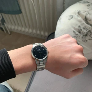 Silverfärgad klocka från Daniel Wellington - Stilren klocka från Daniel Wellington med svart urtavla och silverfärgat armband i metall. Klockan har minimalistisk design utan siffror och DW-logga på urtavlan. Passar perfekt för dig som gillar klassiska accessoarer. OBS Pris Ej Hugget I Sten!