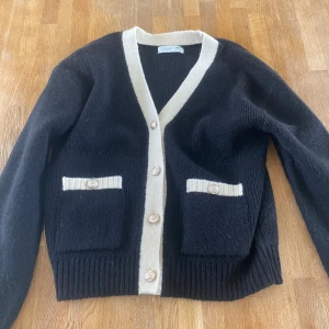 Svart kofta med vita detaljer  - Säljer en svart stickad kofta från primark med vit kant längs knäppningen och vid fickorna. Koftan har långa ärmar, två fickor framtill och knappar i guld. Köparen står för frakt!