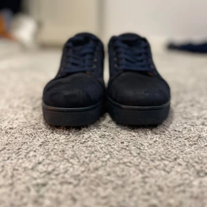 Marinblå  mockasneakers från Christian Louboutin - Säljer ett par mörkblå sneakers från Christian Louboutin i mocka med klassisk röd sula. Skorna har rund tå, platt sula och snörning. Kommer med originalkartong och dustbag. Perfekta för dig som vill ha något stilrent men ändå lyxigt.Pris kan diskuteras och kvittot följer med,byten funkar.