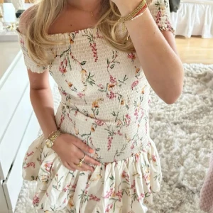 Hm klänning  - Supersöt offshoulder klänning i ljusbeige med blommigt mönster i rosa, grönt och gult. Använd 1 gång! Lånad bild! Skriv vid intresse!🩵