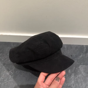 Svart skepparmössa från H&M - Stilren svart skepparmössa från H&M med klassisk form och böjd skärm. Tillverkad i mjukt tyg som ger en bekväm passform. Perfekt accessoar för att lyfta din outfit! Aldrig använt 