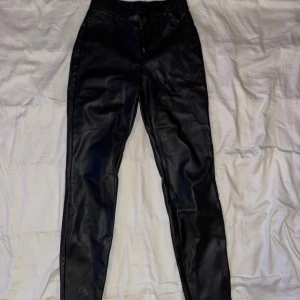 Svarta skinnbyxor från Zara - Snygga svarta skinnbyxor från Zara med hög midja och smal passform. Byxorna har klassisk femficksdesign och stängs med dragkedja och knapp. Perfekta för en trendig och edgy look.