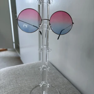 Runda solglasögon med rosa-blått glas - Säljer ett par runda solglasögon med tunn metallbåge och färgade glas i rosa och blått. Glasen har en snygg gradient från rosa upptill till blått nedtill. Perfekt accessoar för dig som vill sticka ut.