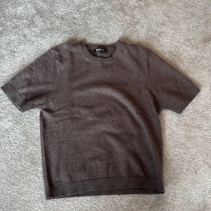 Brun kortärmad tröja från Gina Tricot - Säljer en brun, mjuk och stilren kortärmad tröja från Gina Tricot. Tröjan har rund halsringning och ribbade kanter vid ärmslut och nederkant. Perfekt för lager-på-lager eller sommarens alla outfits.