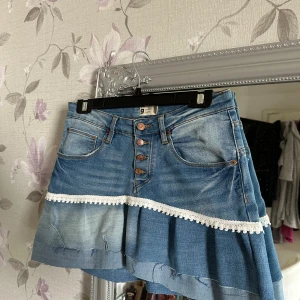 Jeanskjol med volang och spetsdetalj - Supersöt volang kjol med en super söt spetsdetalj, jag har sytt kjolen själv så inte perfekt men väldig fin och unik, den har ett stretchigt material, skriv om ni har några frågor💕 Midjemått 37cm