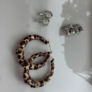 Mix av örhängen  - Säljer ett set med stora bambu-inspirerade hoops i guld och svart, ett par små silvriga örhängen med stenar samt en örhängen med flätad design. Perfekt för dig som gillar att variera dina accessoarer.