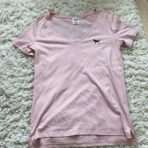 Ljusrosa t-shirt från Victoria's Secret PINK - Ljusrosa t-shirt från Victoria's Secret PINK med v-ringning och korta ärmar. Framsidan har en liten svart hund i paljetter och baksidan texten 'LOVE PINK' i paljetter. Skön bomullskvalitet, perfekt för en avslappnad stil💕💕