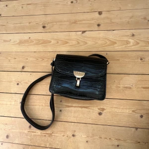 Svart axelväska  - Svart axelväska med guld detalj. 