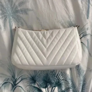 Vit quiltad axelväska - Säljer en stilren vit axelväska med quiltat mönster och dragkedja upptill. Perfekt att bära över axeln för en clean och modern look. Väskan har en enkel design som passar till många outfits. Vill få såld då jag måste ha min garderob ut rensad omgående! 🥰💖