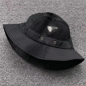 Svart bucket hat från Prada - Stilren svart bucket hat från Prada med nätpaneler och metallogo framtill. Hatten har rund form och bred brätte, perfekt för en trendig look. Tillverkad i syntetmaterial med ventilerande detaljer.