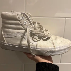 Vita höga sneakers från Vans - Säljer ett par klassiska vita höga sneakers från Vans med snörning. Perfekta nu till studenten för ursprung, flaket eller mottagningen!! (Har ej tvättat dessa men är säker på att fläckarna som finns går bort me lite vanish, i överlagt är de endast använda enstaka gånger)