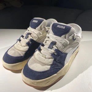 Puma sneakers i beige och blå - Snygga Puma sneakers i en kombination av beige och blå. Skorna har en klassisk design med snörning och en bekväm sula. Perfekta för en avslappnad stil.