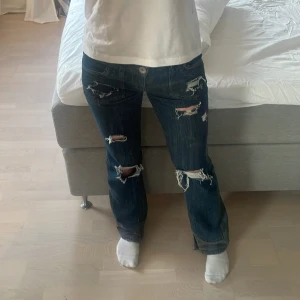 Mörkblå jeans med slitningar och nitar - Snygga mörkblå jeans från Lucky Esprit med coola slitningar på framsidan och nitar längs bakfickorna. De har en låg midja och en straight passform. Säljer dom för har tröttnat på dom. Innebens längden är 79 och midjemåttet är 37