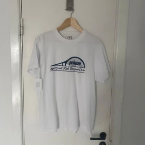 Vit t-shirt från Sporty & Rich - Säljer en helt ny vit t-shirt från Sporty & Rich med tryck på framsidan som säger 'Sports and Rich Racquet Club'. T-shirten har en klassisk passform och är kortärmad. Perfekt för en avslappnad stil. Passar M utmärkt! Skriv om ni har några övriga frågor🙌