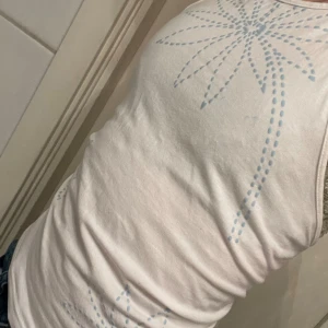 Vit linnetopp från HPO Collection - Säljer en vit linnetopp från HPO Collection med ljusblått blommönster. Toppen har smala axelband som knyts i nacken och en bekväm passform. Perfekt för varma dagar!