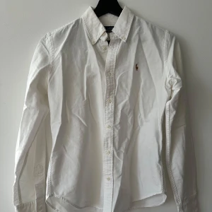 Vit skjorta från Ralph Lauren - Säljer en stilren vit skjorta från Ralph Lauren i super slim fit. Skjortan har långa ärmar och klassiska knappar framtill. Den är prydd med det ikoniska broderade logotypen på bröstet. Perfekt för en elegant look.