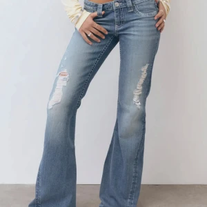 Blå bootcut jeans med slitningar - Snygga blå bootcut jeans med slitningar på låren. Perfekta för en avslappnad stil. De har en klassisk femficksdesign och en knappgylf.