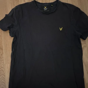 Svart t-shirt från Lyle & Scott - Säljer en svart t-shirt från Lyle & Scott med deras ikoniska gula logga broderad på bröstet. T-shirten har en klassisk passform och är kortärmad, perfekt för en stilren look. Skön och enkel att matcha med det mesta. 🖤