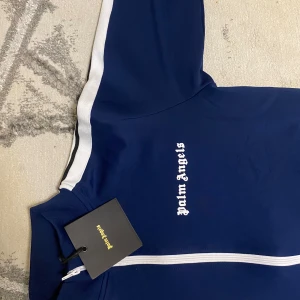  Parm Angeles mörkblå  - Säljer en sprillans ny Palm Angels tracksuit i marinblått med vita stripes. Helt oanvänd, lapparna sitter kvar och kvaliteten är på topp. En perfekt kombination av streetwear och lyx som verkligen sticker ut. Passar både för vardag och fest – ta chansen att äga en av de hetaste tracksuitsen just nu!