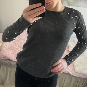 Grå tröja med pärlor från Zara - Snygg grå tröja från Zara dekorerad med pärlor över axlar och ärmar. Tröjan har en rund hals och långa ärmar, perfekt för en stilren look. Passar bra till både jeans och kjol. 🖤
