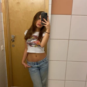 Vit kortärmad t-shirt med draktryck - Säljer en cool vit t-shirt med ett färgstarkt draktryck i rött, svart och gult. T-shirten är kortärmad och har en normal passform. Perfekt för att ge din outfit en edgy touch!