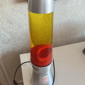 Retro lavalampa i silver och rött - Snygg retro lavalampa med silverfärgad bas och lock. Lampan har en fascinerande kombination av röd lava och gul vätska som skapar ett hypnotiserande ljusspel. Perfekt för att ge rummet en cool vintagekänsla. Ansluts med svart sladd.